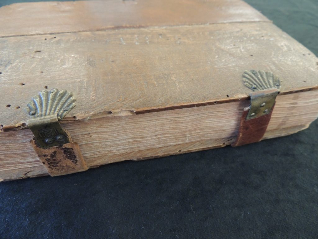 Side view of old rare book bound with wooden boards held together by seashell shaped clasps.