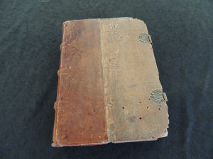 Cover of book shows leather covering one half of the book going around the spine. The other half is an exposed wood board with clasps holding it closed. The wood board has a number of small holes about a milimeter in diamter..