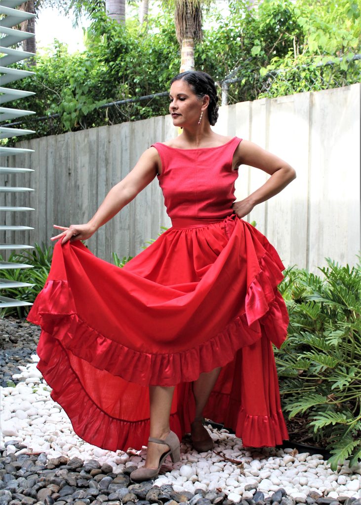 Mujer posando con un vestido rojo Bomba con plantas detrás de ella