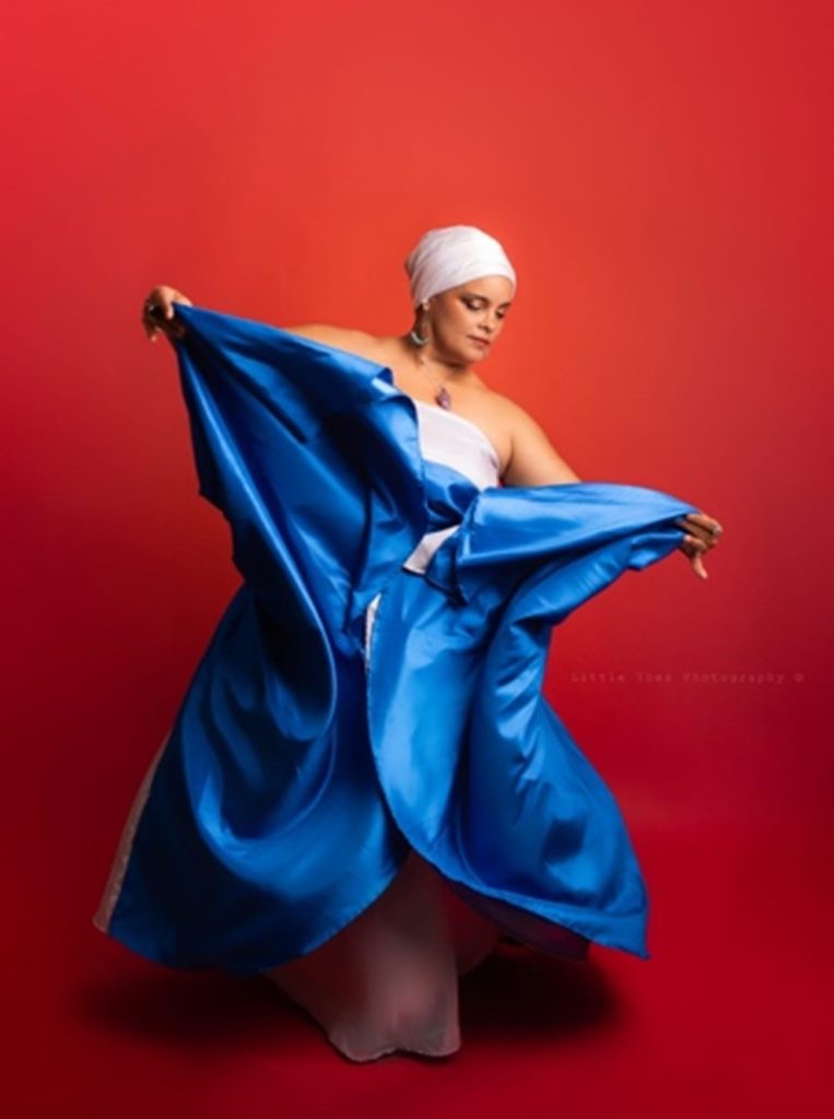 Woman posing with her blue Bomba skirt in front of a red background.