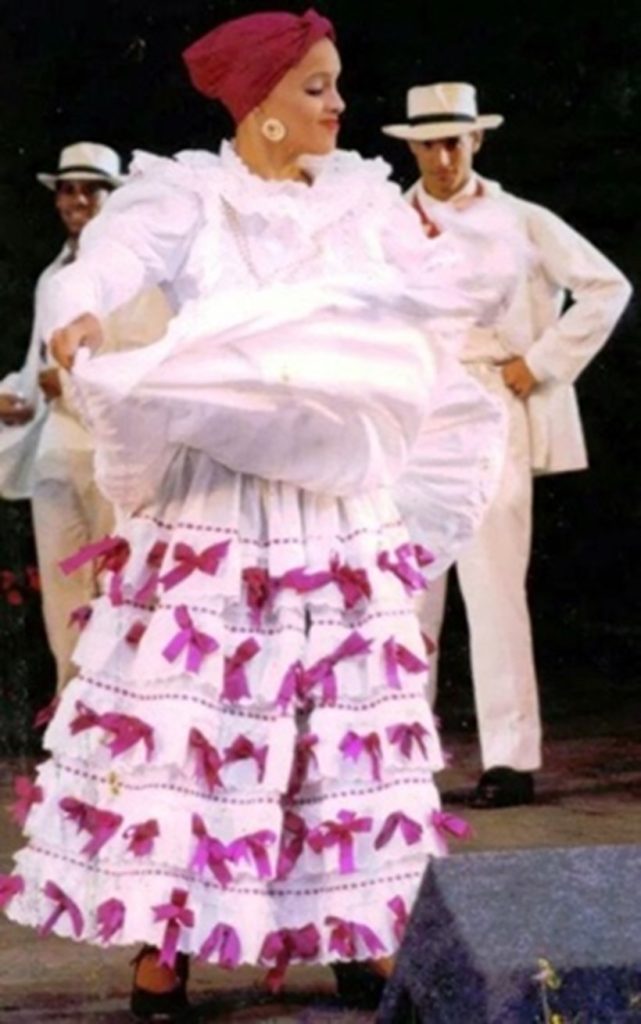 Una mujer con un vestido de Bomba blanco con lazos rosas.