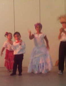 Children on a stage waving while wearing traditional costumes