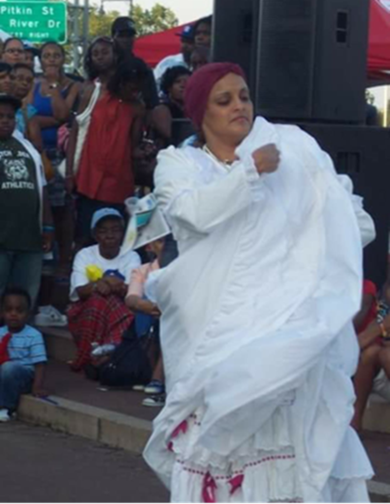 Una persona con un traje de Bomba blanco bailando con espectadores detrás.