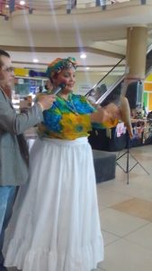 Mujer vestida con una falda blanca y una blusa colorida hablando por un micrófono