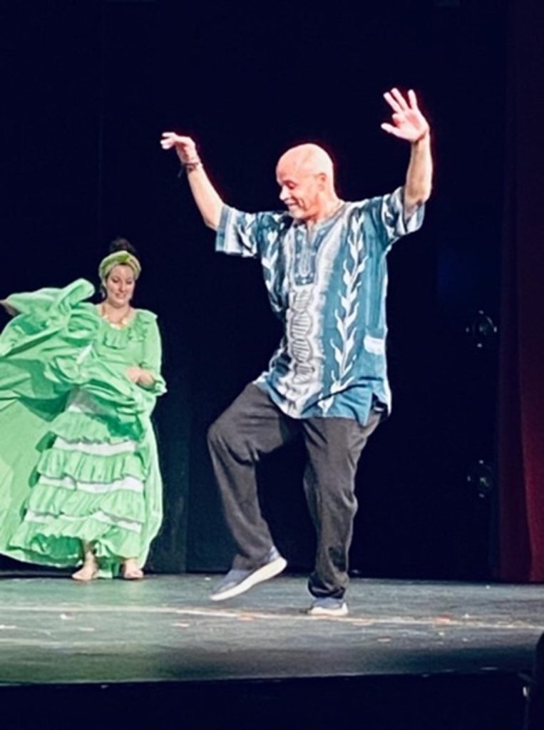 A man dancing on a stage with a woman in a green dress in the background