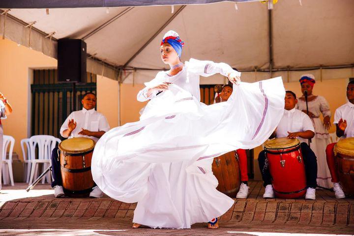 Una bailarina en un traje blanco de Bomba bailando frente a musicos