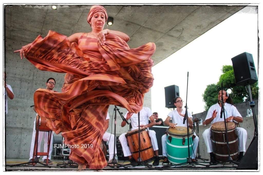 A female performer dancing on stage in front of musicians in a red Bomba outfit