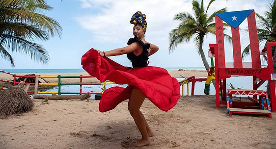 Mujer bailando en una falda roja y un pańuelo colorido en la playa