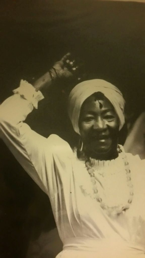 An older woman wearing a white Bomba dress with her right arm raised