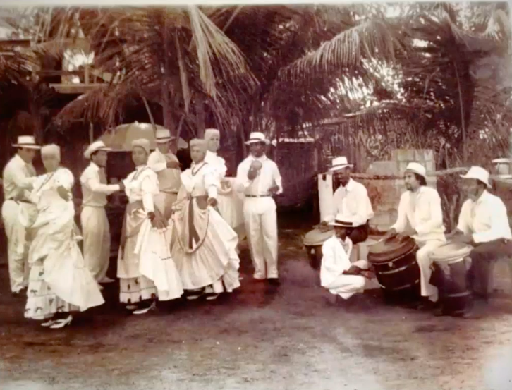 Un grupo de personas posando en la playa vestidos en el traje tradicional de Bomba