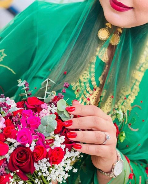 Close up of woman holding flowers with painted nails. She is wearing a fitted top and sheer-shawl.