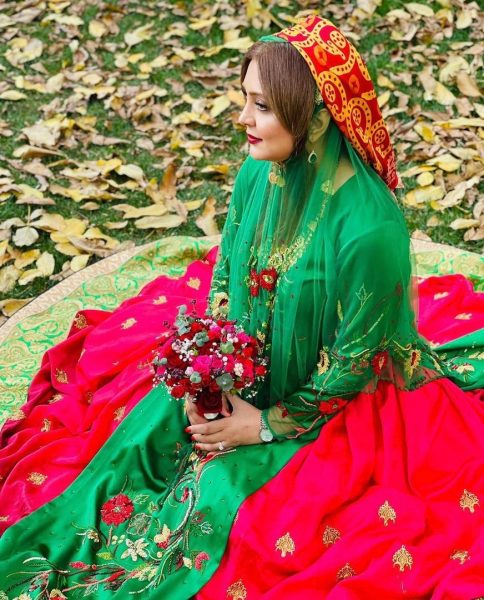 Close-up of woman sitting on the ground outside. She is wearing a full length skirt, fitted top, and sheer-shawl.