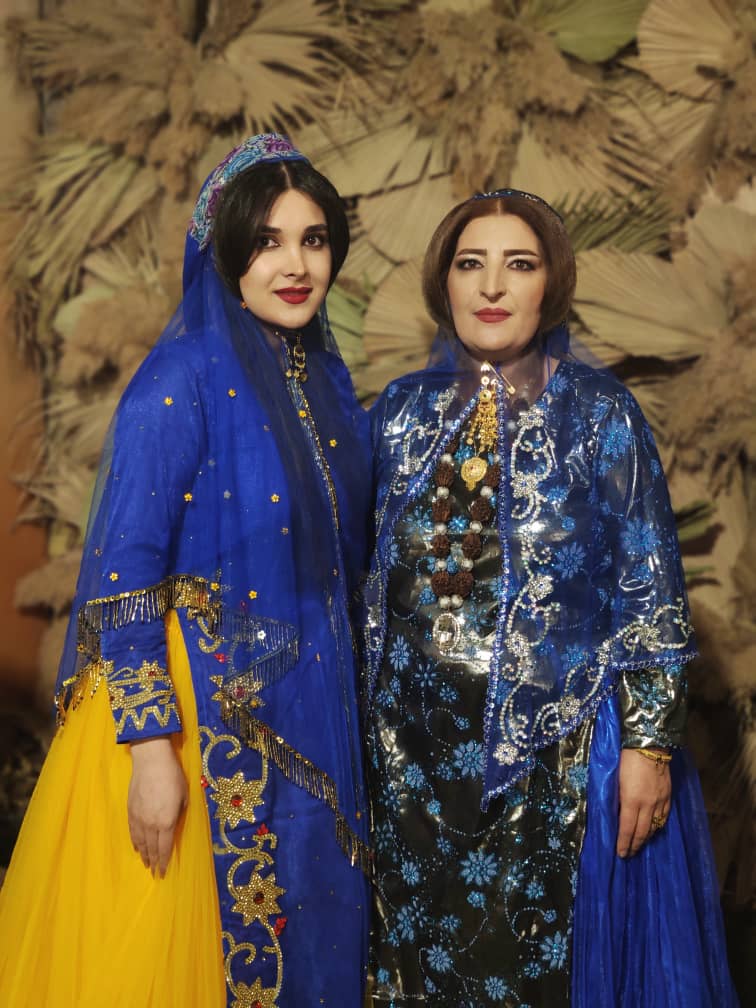 Two women posing while wearing elaborate clothing. The clothing is embellished with beads and sequins.