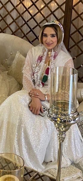Woman sitting on a couch. She is wearing a floor-length skirt and light-weight shawl around her shoulders.