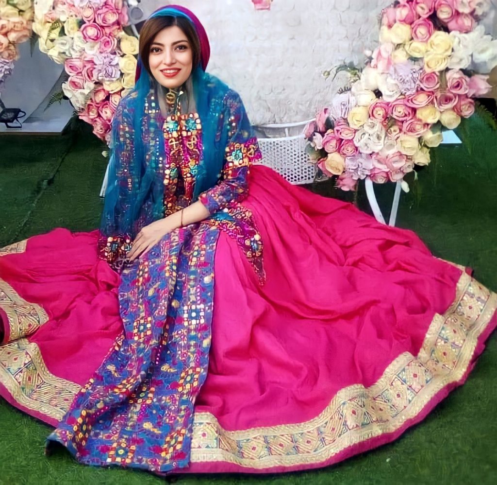 Woman sitting on the floor in front of a ring of flowers. She is smiling at the camera while wearing a floor-length skirt and a light-weight shawl on her shoulders.