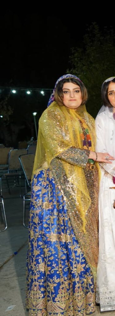 Picture of a woman from head to toe. She is wearing a beaded, floor-length skirt and a light-weight shawl. She is looking at the camera.