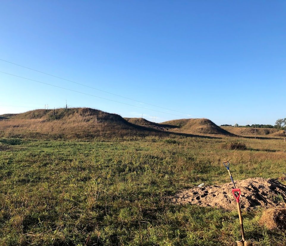 Mounds within a flat landscape with a blue sky in the background.