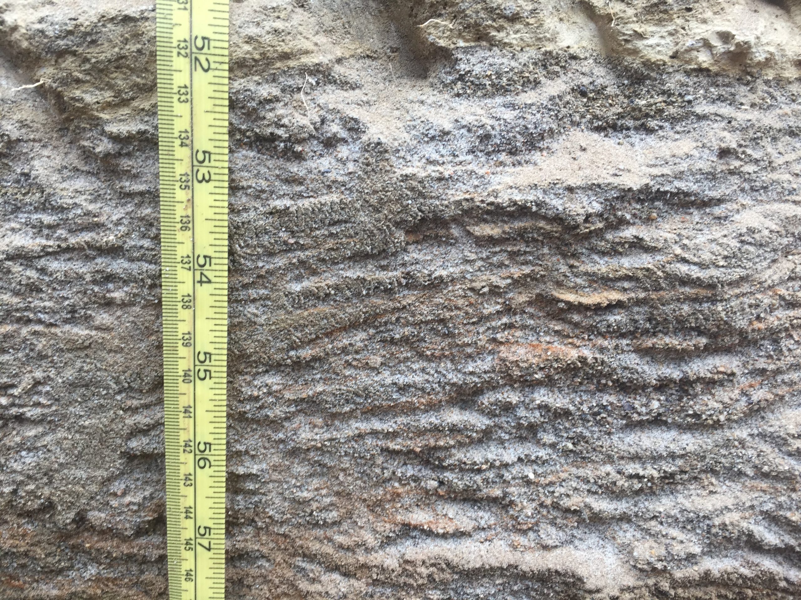 A soil profile with thin stacked layers that are only a couple millimeters thick of different textures. There are redox (orange) features throughout the profile.