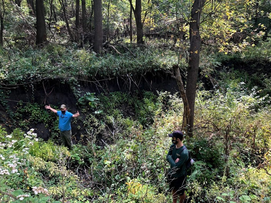 Two people standing in a gully located in a forested areas near Ames High School.