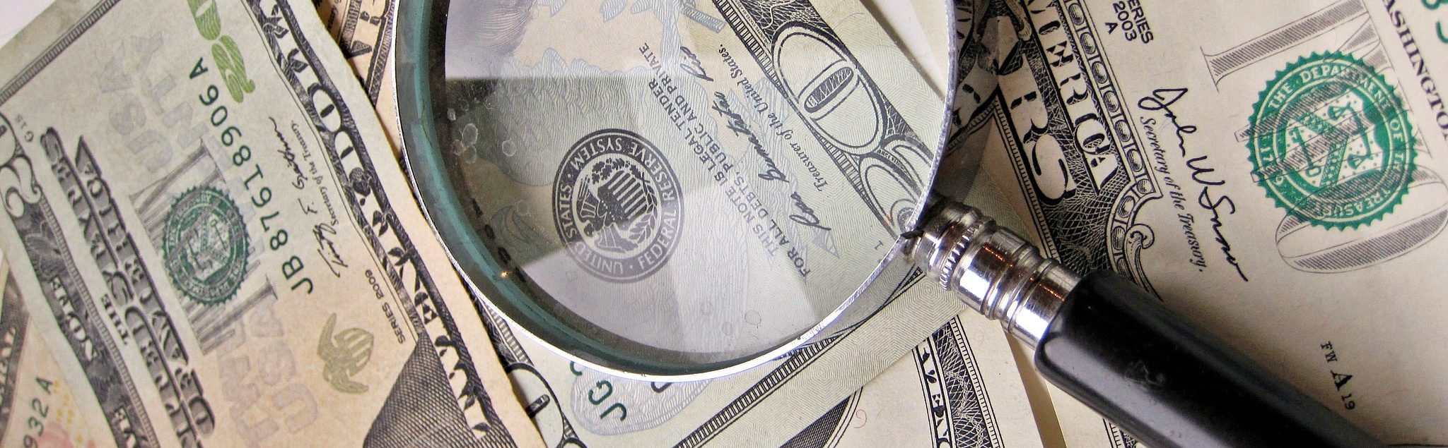 A magnifying glass on a stack of money.