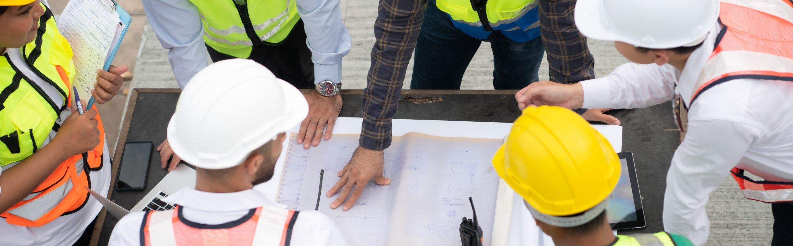 A group of workers wearing safety vests and helmets looking at a blueprint