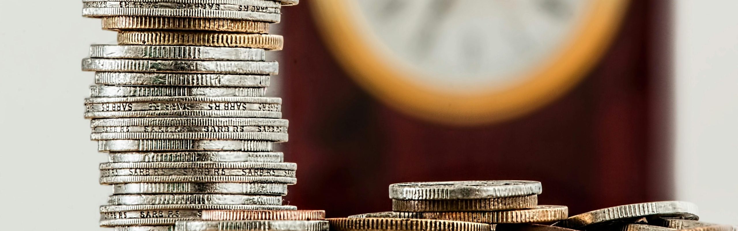 A stock photo of a stack of coins in front of a clock.