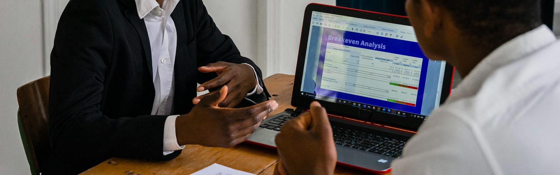 Two businessmen talking in front a a laptop with a breakeven analysis.