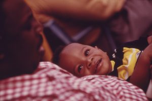 a toddler boy smiles looking up at his father sitting with him