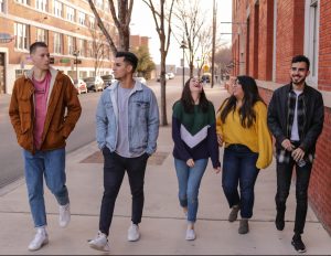 A group of teenagers laughing and talking on the sidewalk.