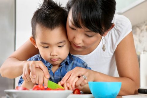 A photograph of a mother helping her young child cut his food.