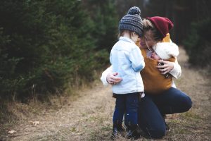 photo of a woman kneeling down with her young child and baby is talking to the child