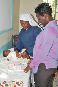 a photo of a mother and her infant at a doctors office. The infant is receiving an immunization shot from a nurse