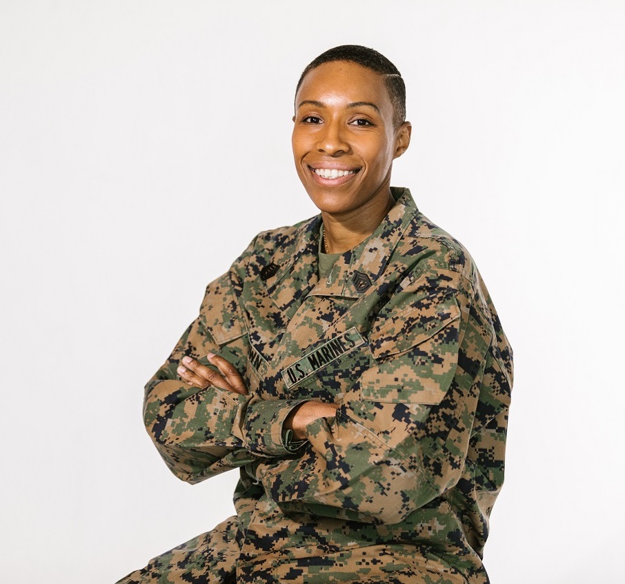 A black soldier smiles at the camera in uniform with her arms crossed.