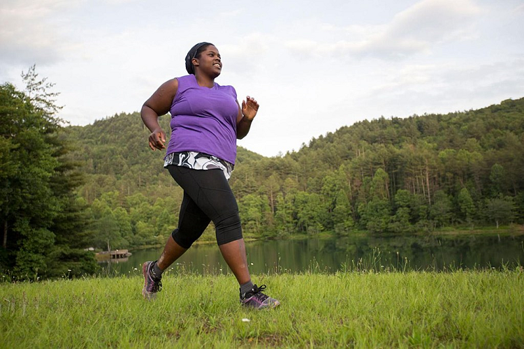 An overweight Black woman jogging in the woods.