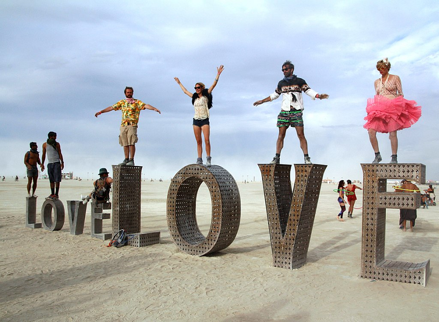 People balanced on large metal letters spelling the word "love." Their dress differs wildly, from fishnets and voluminous skirts to cargo shorts and a Hawaiian shirts.