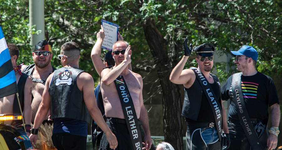 A group of bearded men wearing sunglasses and leather sashes (some shirtless) at a pride parade.