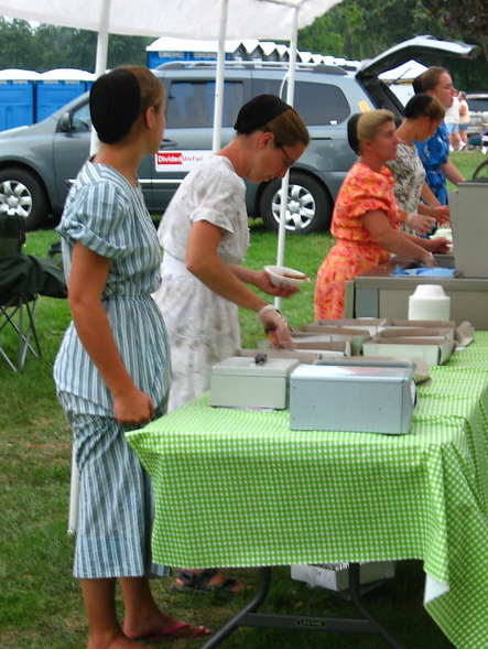 Mennonite women wearing long, colorful printed dresses with their hair covered under a small black hat.