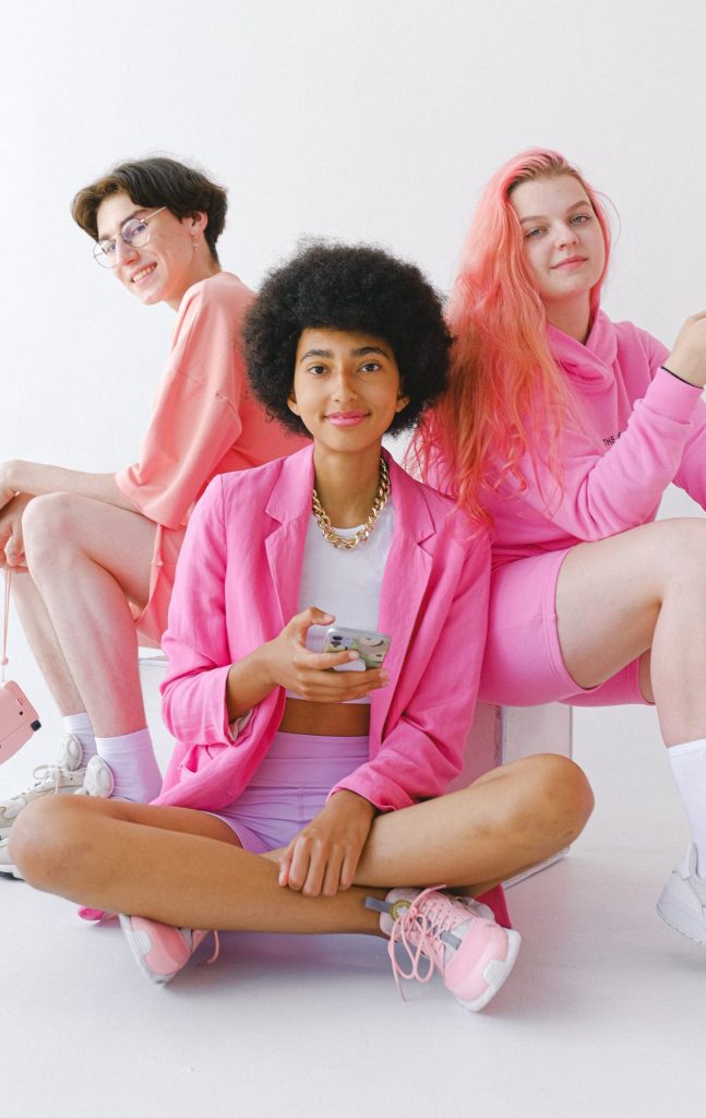 Three teenagers wearing bright pink hoodies, sweatshirts, and blazers over white tops and sneakers.