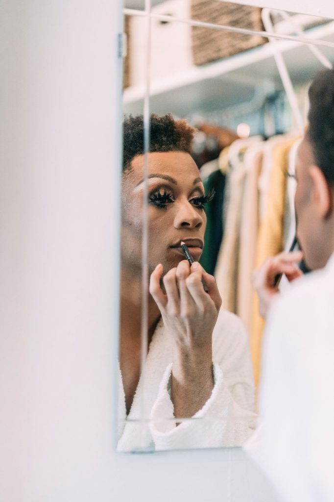 A black man applying lip liner in a mirror for a drag performance.