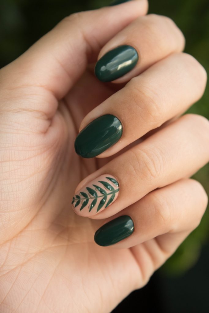 A hand curled inward, showing off painted nails in a dark green with ferns adorning one nail.