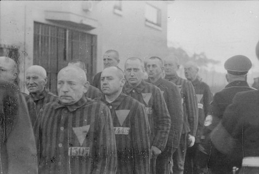 A black and white photo of men in a line wearing striped uniforms with a large triangle over their chest.