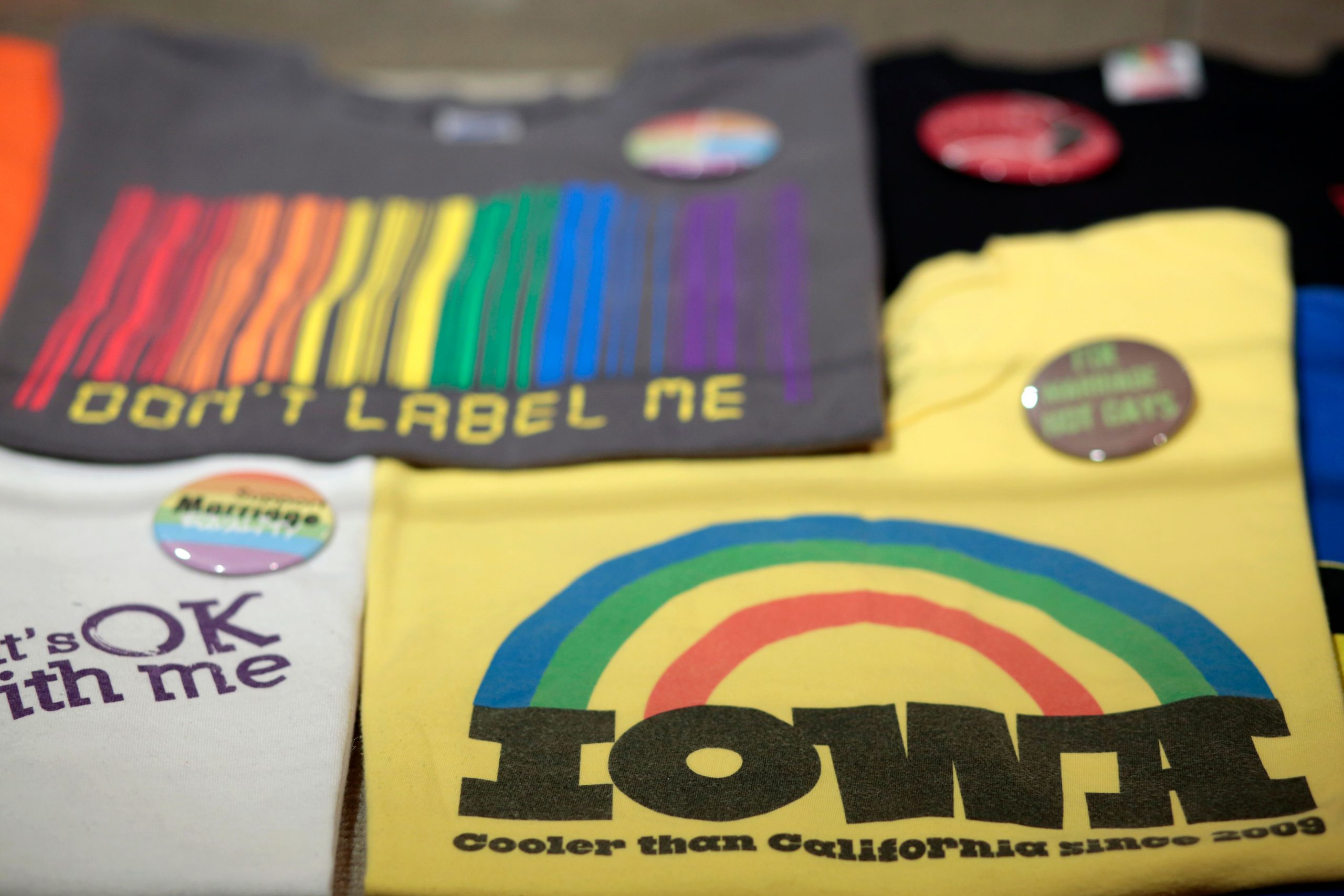 Several t-shirts and buttons from "Overtly Proud" displayed flat in glass case.