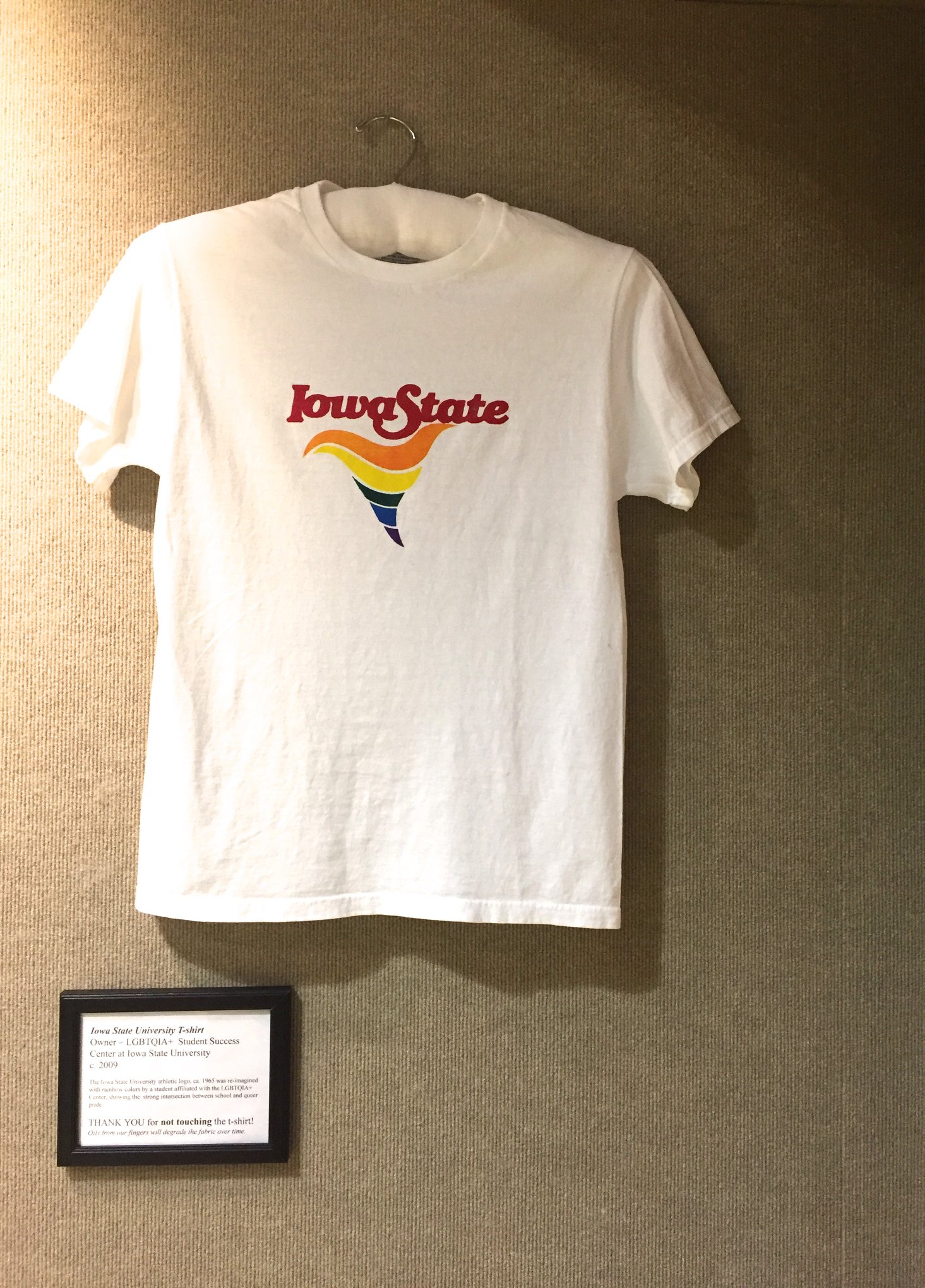 Mounted white short sleeve t-shirt with red text reading: "Iowa State" with a rainbow cyclone underneath
