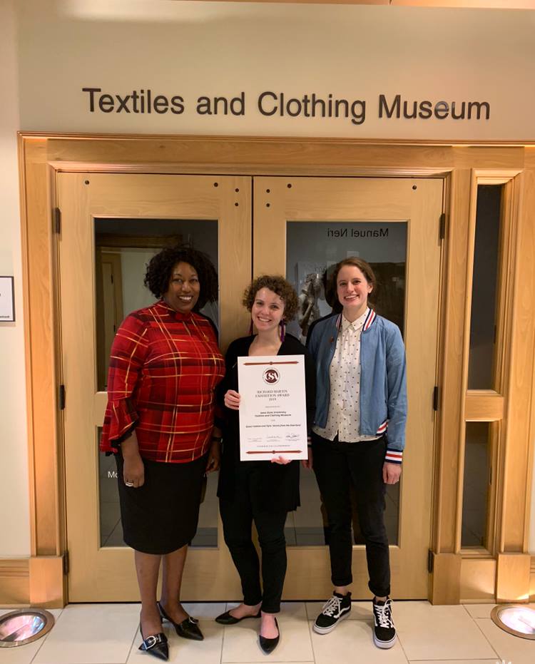 Eulanda Sanders (left), Kelly Reddy-Best (middle), and Dana Goodin (right) in front of the Textiles and Clothing Museum gallery holding the Richard Martin Exhibition Award certificate.
