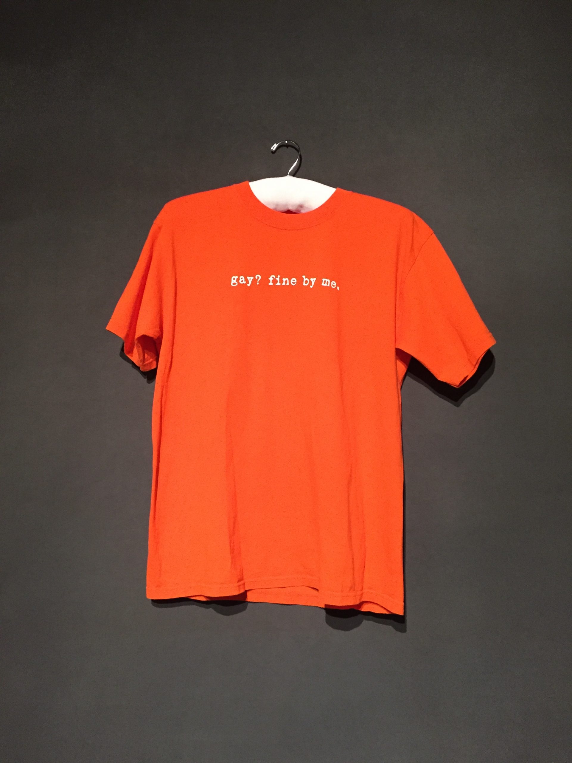 Orange short sleeve t-shirt with white text reading: "gay? fine by me."