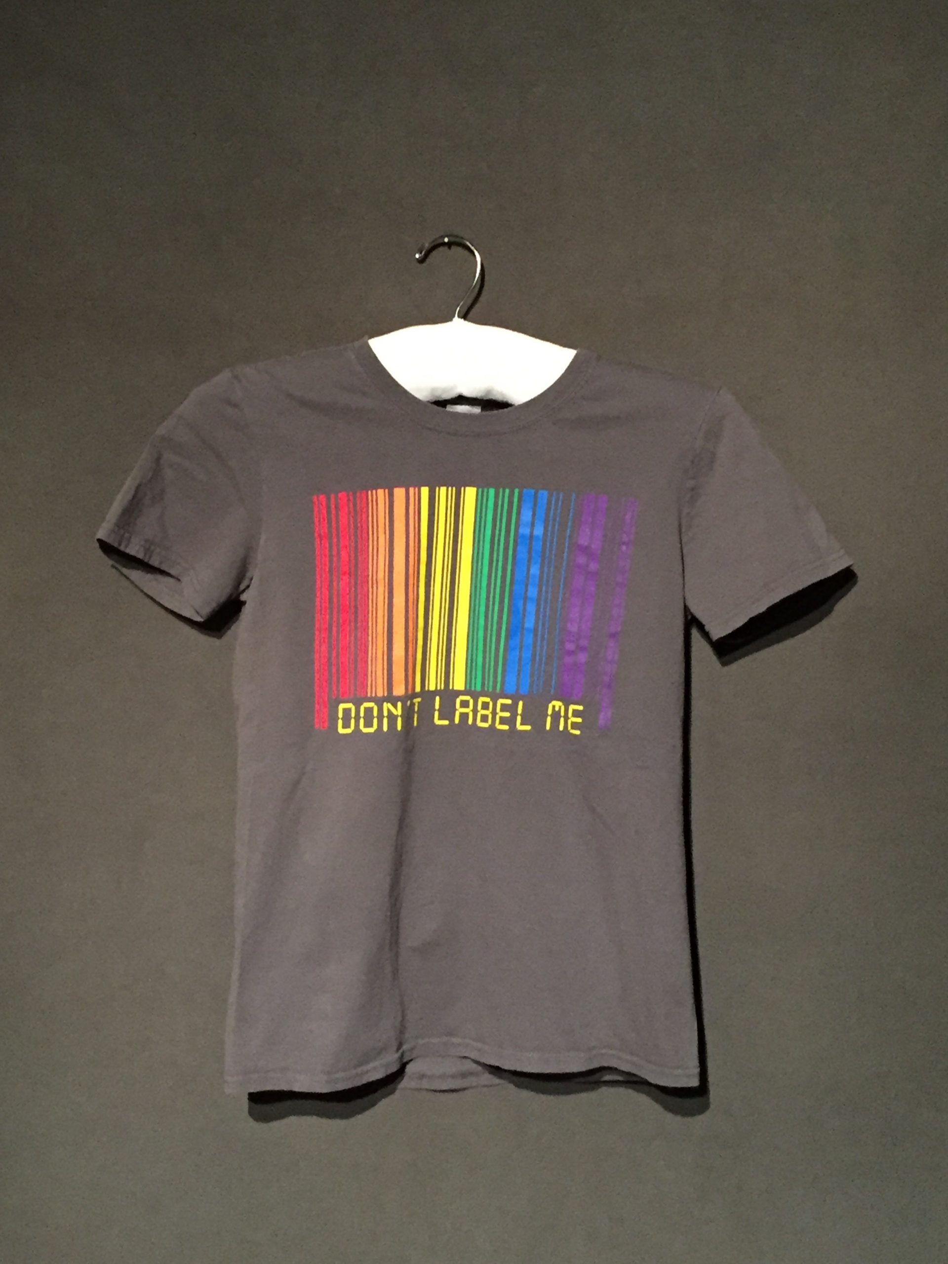 Dark grey short sleeve t-shirt with rainbow barcode and yellow text reading: "Don't Label Me"