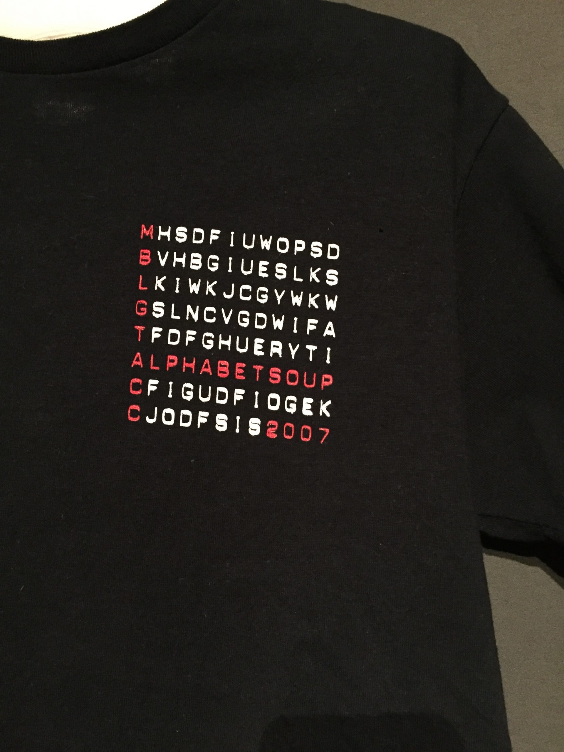 Close-up of black short sleeve t-shirt with red and white text reading: "MBLGTACC Alphabet Soup 2007"