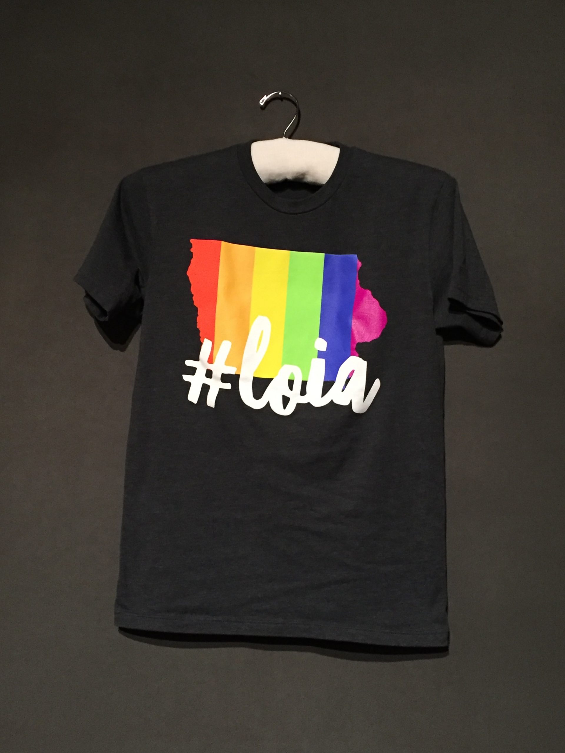 Black short sleeve t-shirt with outline of Iowa state filled in with rainbow, white lettering reading: "#LOIA"