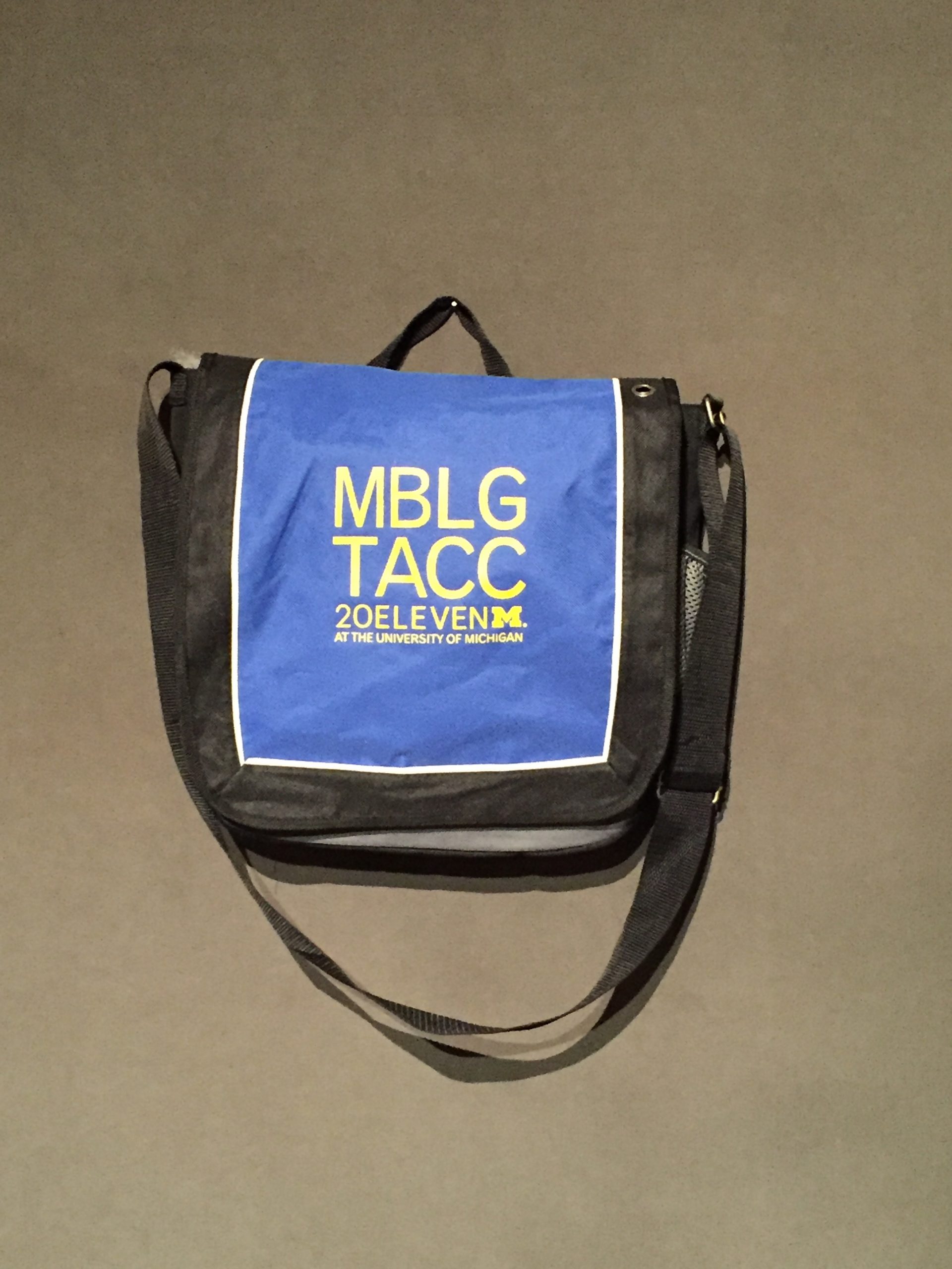 blue and black messenger bag with yellow text reading: "MBLG TACC 20ELEVEN at the University of Michigan"