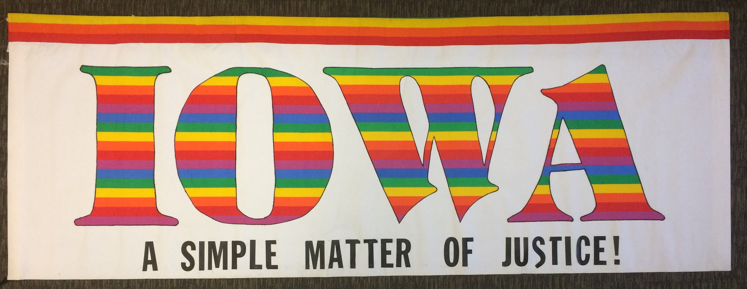 Banner inside of purple bag. Reads: "Iowa: A Simple Matter of Justice!". "Iowa" is in rainbow block lettering and "A Simple Matter of Justice!" in printed with black lettering.